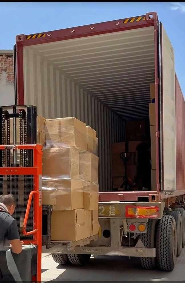 A forklift loading wrapped cartons into a shipping container